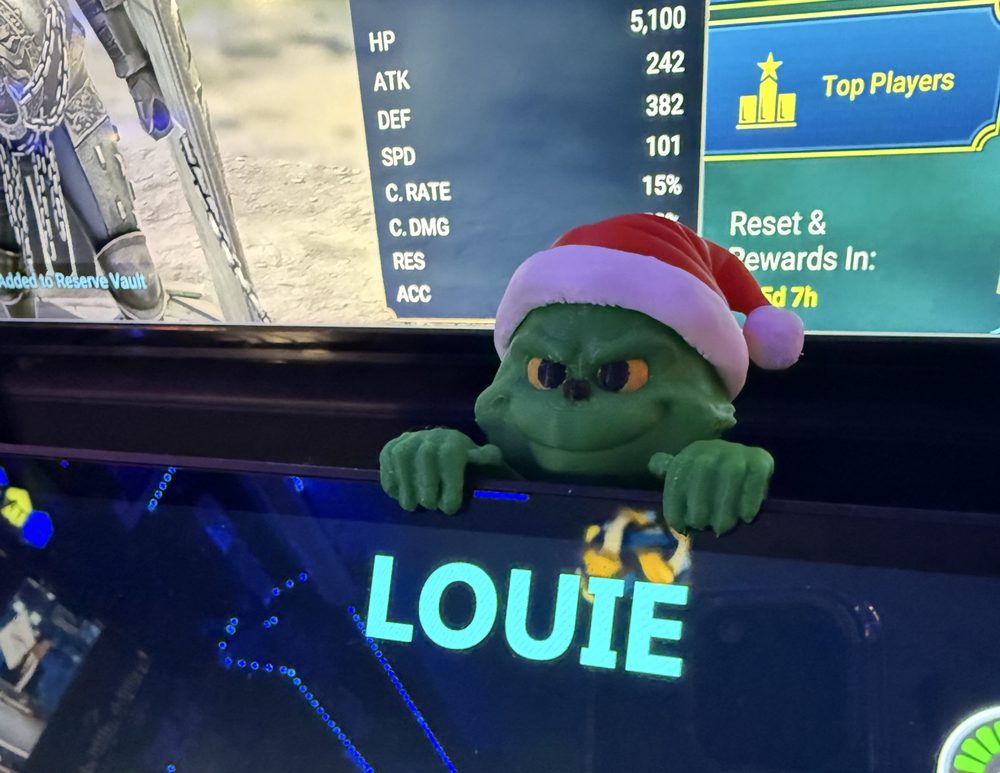 Green Grinch figure in a Santa hat perched on a monitor
